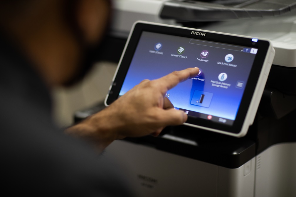 Man touching the screen of a printer as he troubleshoots the device